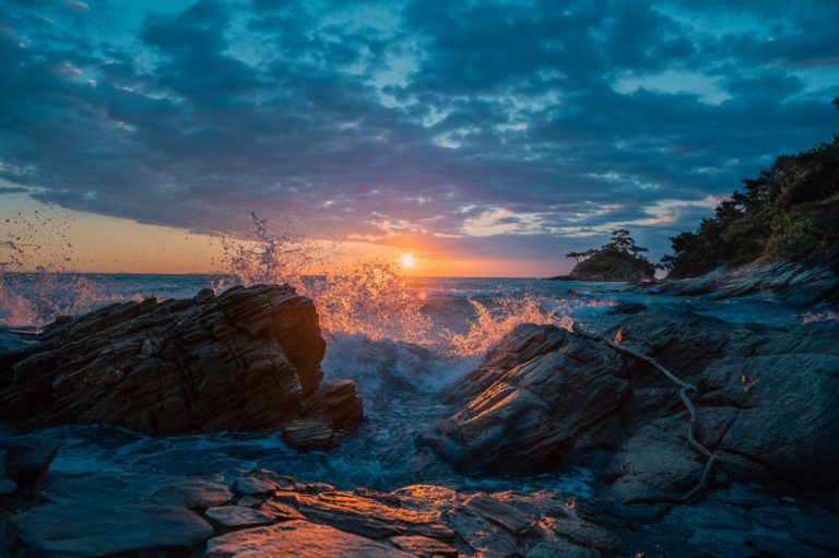 the sun is setting over the ocean as waves crash on rocks