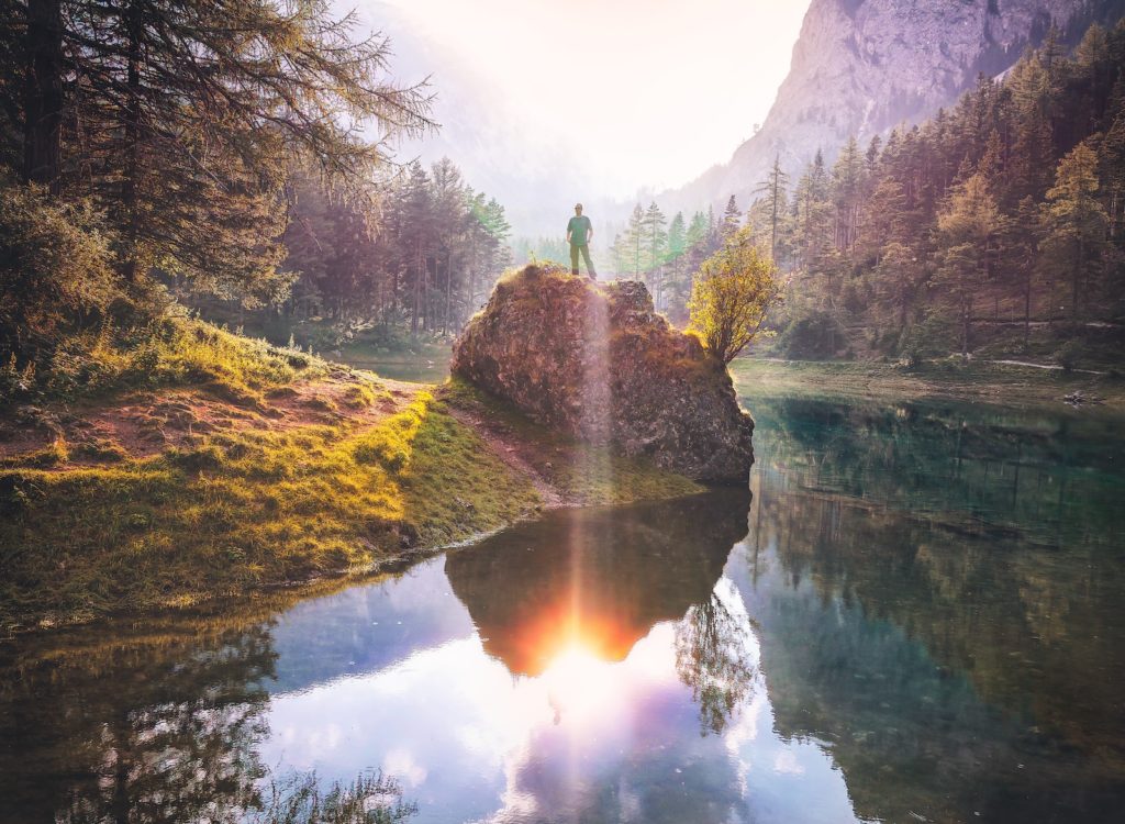 man standing on rock beside lake
